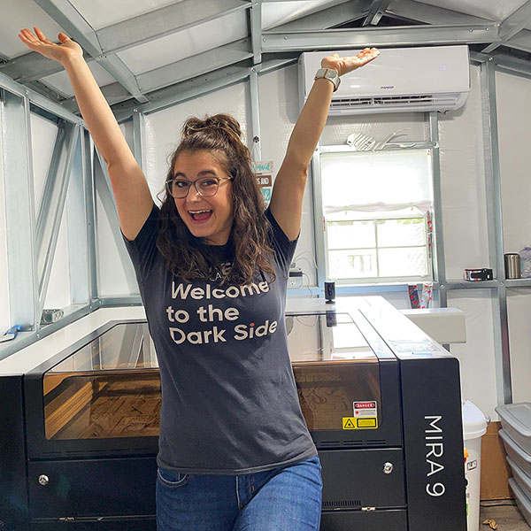 photo of Danielle with her arms raised standing by her Aeon laser, smiling