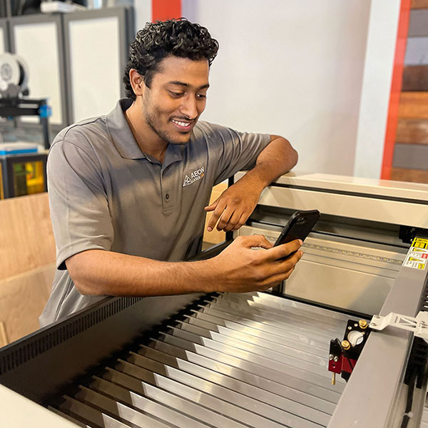 photo EJ standing over a laser while video chatting with a customer on his mobile phone