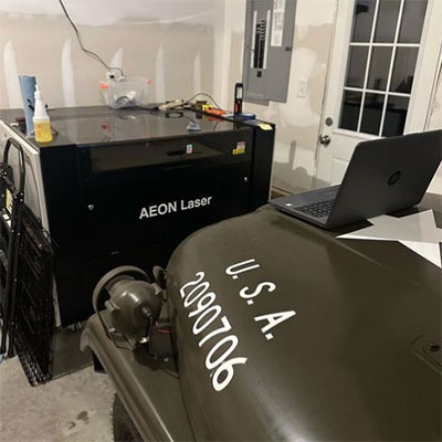 Aeon NOVA Laser in the garage accross from a Jeep with a laptop on top