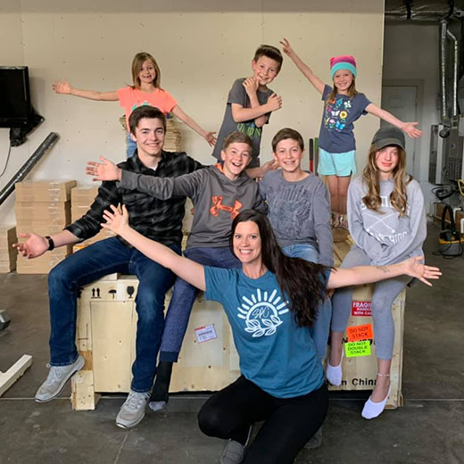 family of eight, with big smiles and extended arms, posing around a giant crate containing an Aeon CO2 laser inside.