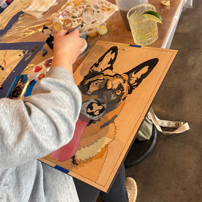 person painting a custom cut wooden portrait of a dog