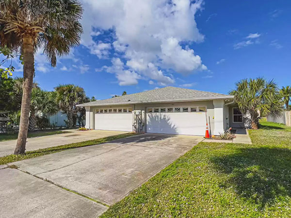  photo of a duplex with two garages, long driveways, green lawn and palm trees, on a sunny day