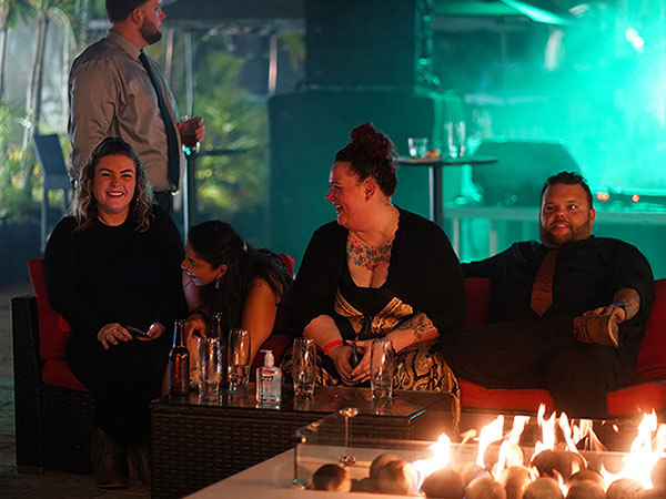 three people in evening wear sitting in front of a fire and smiling 