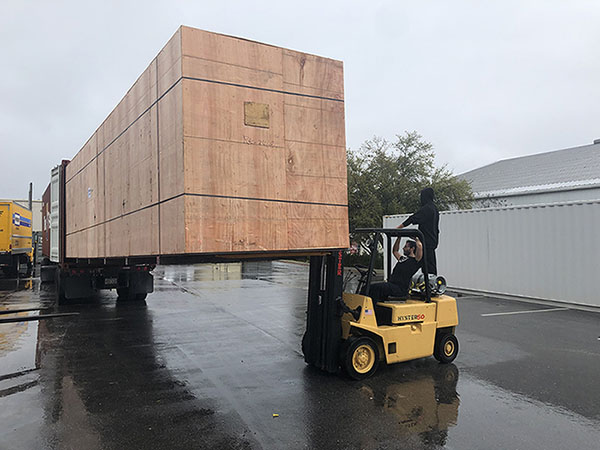 a yellow forklift pulling a giant 40 ft long container out of a truck